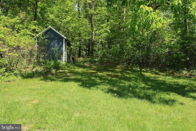 view of grassy yard featuring an outbuilding and a wooded view
