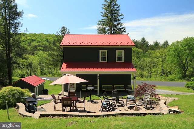 rear view of property featuring metal roof, a patio area, a fire pit, a forest view, and a yard