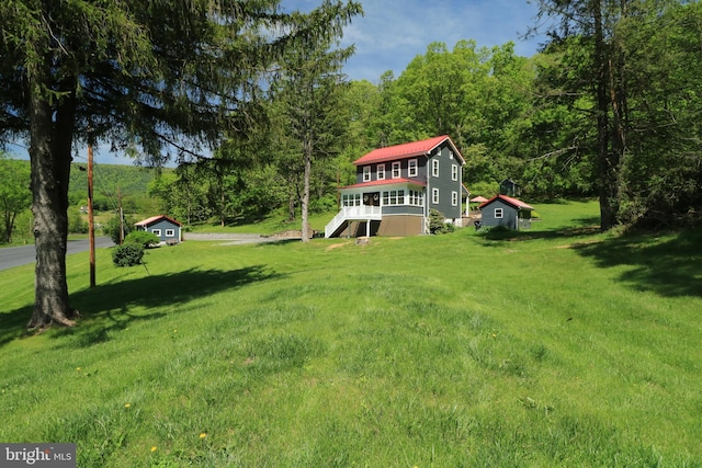 view of green lawn with stairs, a wooded view, and a wooden deck