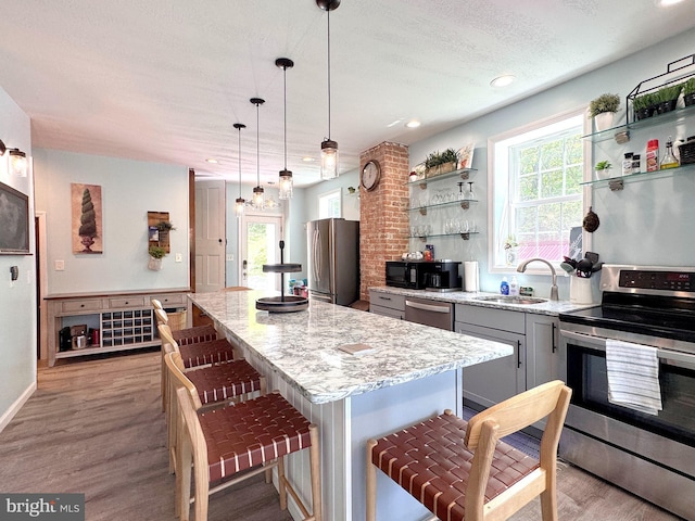 kitchen with stainless steel appliances, a sink, a center island, wood finished floors, and a kitchen breakfast bar