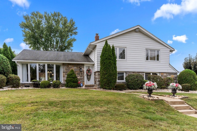 tri-level home with stone siding, a chimney, and a front yard