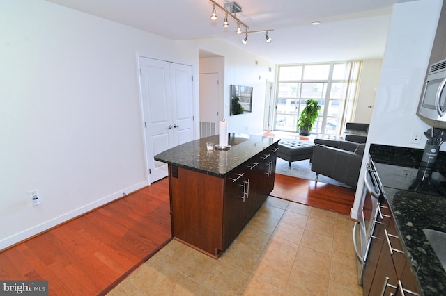kitchen with stainless steel appliances, open floor plan, a kitchen island, dark stone counters, and baseboards