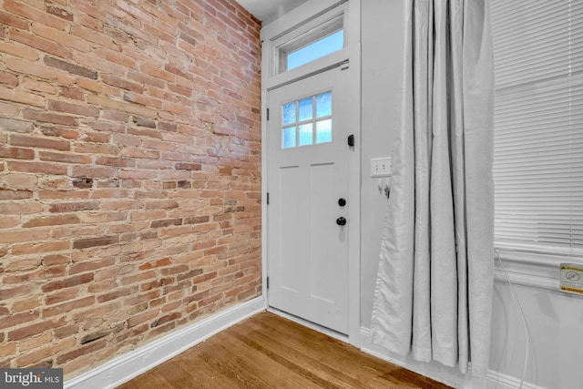 entryway featuring wood finished floors, baseboards, and brick wall