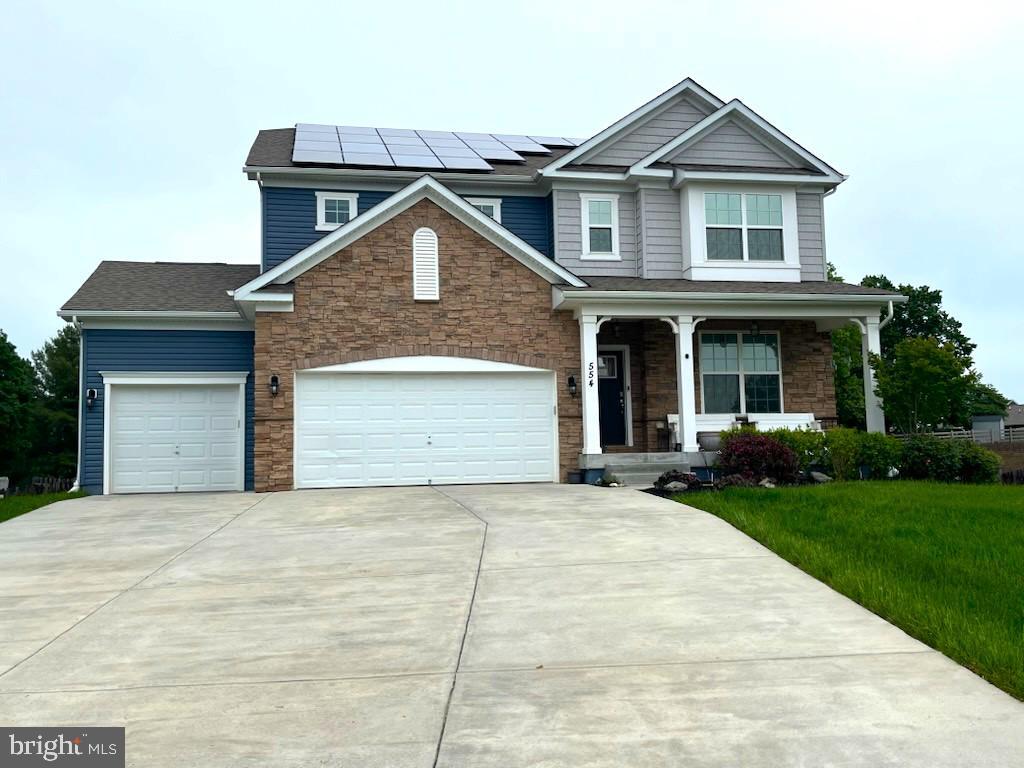 view of front of house featuring covered porch, stone siding, concrete driveway, and a garage