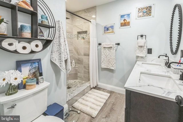 full bath with wood finished floors, toilet, tiled shower, baseboards, and double vanity