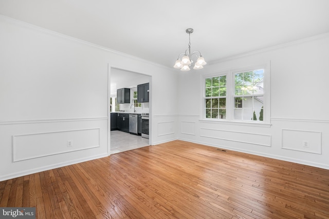 spare room with a chandelier, crown molding, light wood finished floors, a wainscoted wall, and a decorative wall