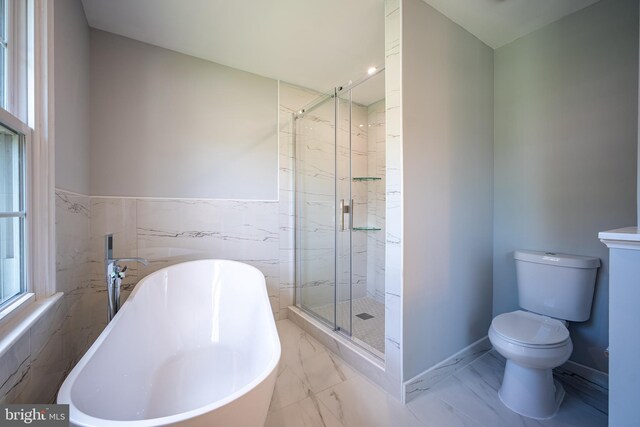 full bathroom with marble look tile flooring, toilet, a shower stall, a freestanding tub, and tile walls