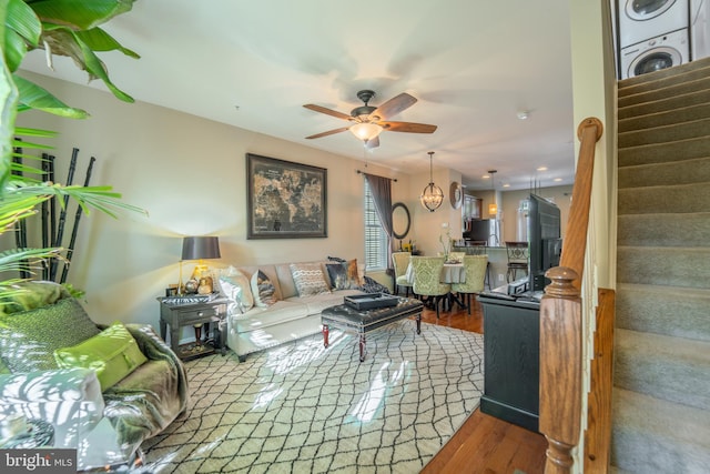 living room featuring stacked washer and clothes dryer, stairway, wood finished floors, and a ceiling fan