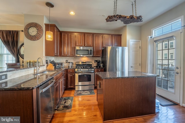 kitchen with appliances with stainless steel finishes, a sink, dark stone countertops, a center island, and hanging light fixtures