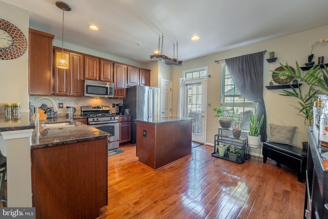 kitchen with appliances with stainless steel finishes, a sink, a center island, dark stone counters, and light wood-type flooring