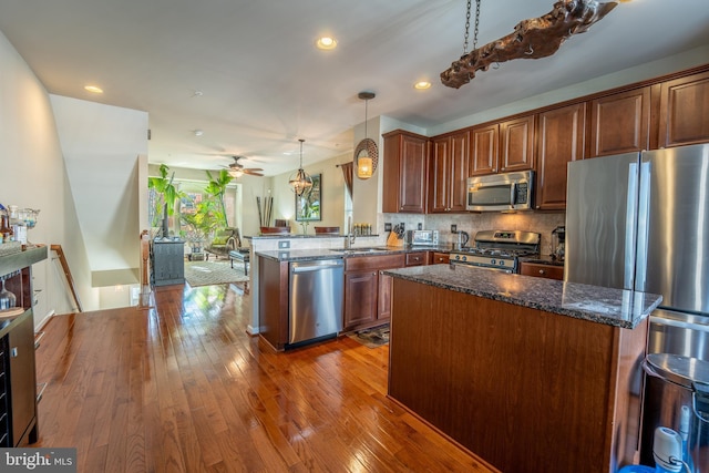 kitchen with stainless steel appliances, ceiling fan, dark stone counters, a peninsula, and recessed lighting