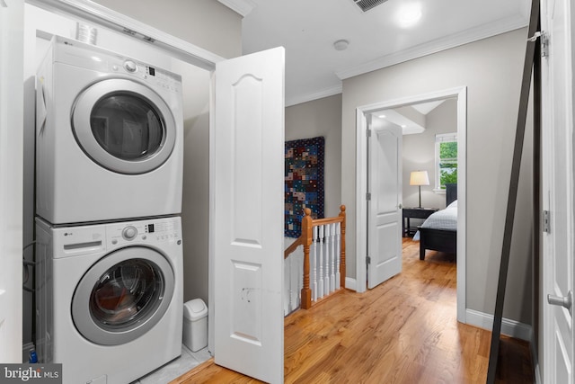 washroom featuring stacked washer / dryer, light wood finished floors, crown molding, and baseboards