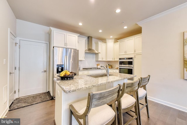 kitchen featuring wall chimney range hood, stainless steel appliances, a sink, wood finished floors, and recessed lighting