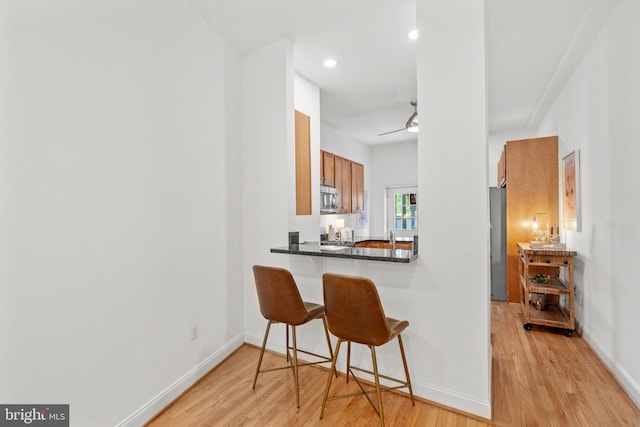 kitchen featuring stainless steel appliances, light wood-type flooring, a kitchen breakfast bar, brown cabinetry, and dark countertops