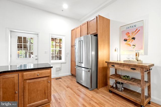 kitchen with high quality fridge, light wood-style flooring, dark stone counters, and brown cabinets