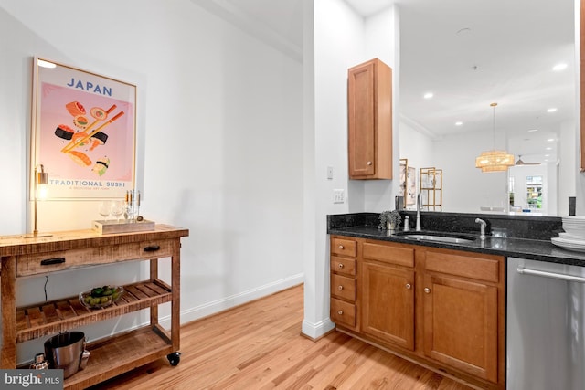 kitchen featuring stainless steel dishwasher, a sink, light wood-style floors, brown cabinetry, and dark stone countertops