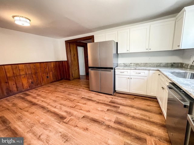1021 Park Ave, Annapolis, MD 21403 - kitchen with stainless steel appliances, light wood-style flooring, white cabinets, a wainscoted wall, and wood walls