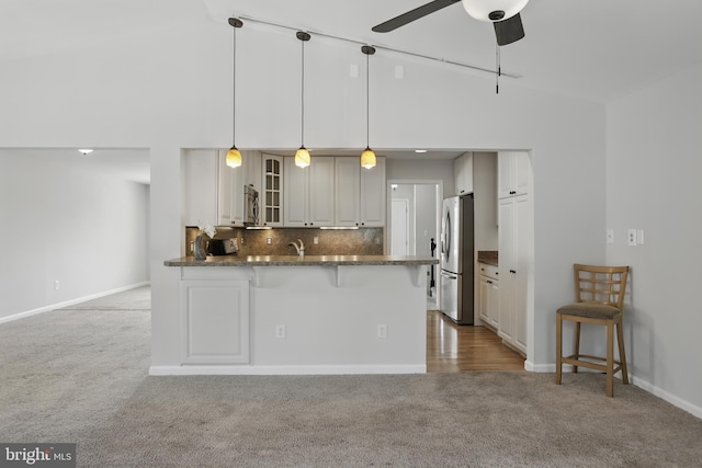kitchen featuring light carpet, stainless steel appliances, a peninsula, glass insert cabinets, and a breakfast bar area
