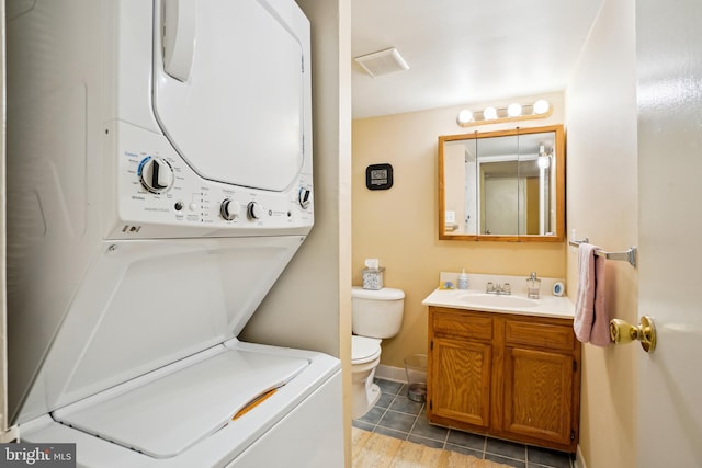 bathroom with stacked washer / drying machine, toilet, vanity, tile patterned floors, and baseboards