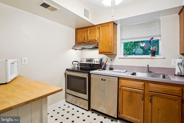 kitchen with stainless steel appliances, a sink, under cabinet range hood, and brown cabinets