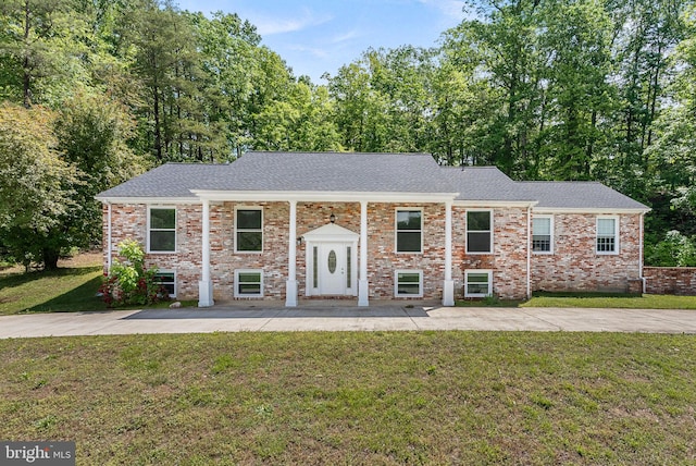 split foyer home with a front lawn, brick siding, and roof with shingles
