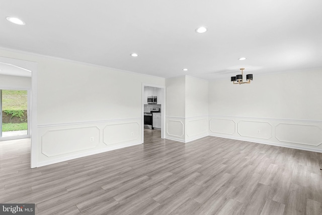 empty room featuring a decorative wall, recessed lighting, ornamental molding, a chandelier, and light wood finished floors