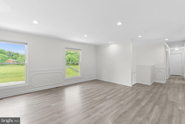 unfurnished living room featuring light wood-style flooring, recessed lighting, a wainscoted wall, ornamental molding, and a decorative wall