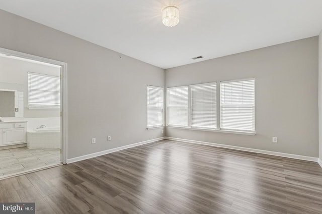 unfurnished bedroom with wood finished floors, baseboards, and ensuite bathroom