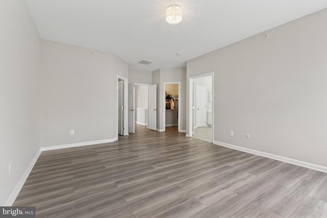 unfurnished bedroom with wood finished floors, baseboards, a spacious closet, and a closet