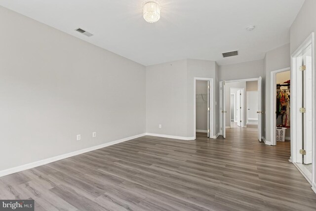 unfurnished bedroom with a spacious closet, wood finished floors, a closet, and baseboards
