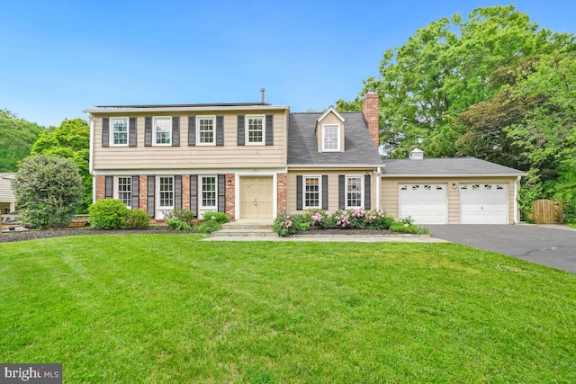 colonial-style house with asphalt driveway, a chimney, a front yard, and a garage