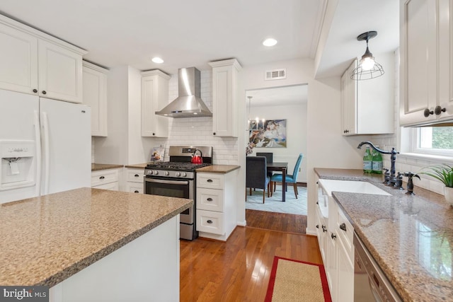 kitchen featuring wall chimney range hood, stainless steel appliances, backsplash, white cabinetry, and recessed lighting