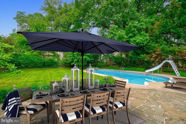 swimming pool with a patio, outdoor dining space, a water slide, and a lawn