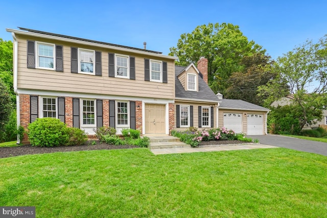 colonial-style house with asphalt driveway, a chimney, a front yard, a garage, and brick siding