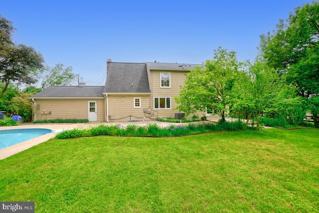 rear view of house with a lawn, an outdoor pool, cooling unit, a patio area, and a chimney