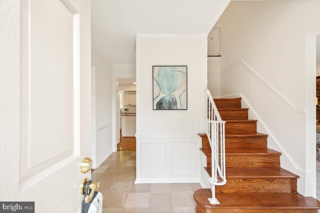 staircase featuring a decorative wall, ornamental molding, tile patterned flooring, and wainscoting