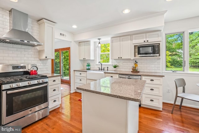 kitchen featuring stainless steel range with gas cooktop, wall chimney range hood, backsplash, white cabinetry, and recessed lighting