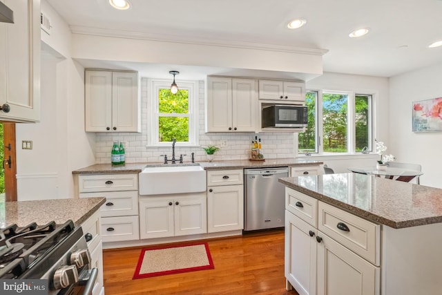 kitchen featuring stainless steel appliances, a sink, tasteful backsplash, light wood-type flooring, and light stone counters