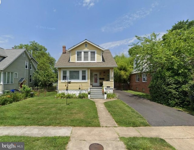 bungalow-style house with a chimney, a front yard, and roof with shingles