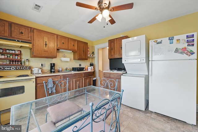 kitchen featuring white appliances, stacked washer / dryer, under cabinet range hood, a ceiling fan, and brown cabinets