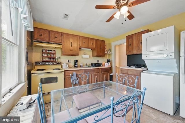 kitchen featuring electric stove, stacked washer / dryer, under cabinet range hood, brown cabinetry, and a ceiling fan