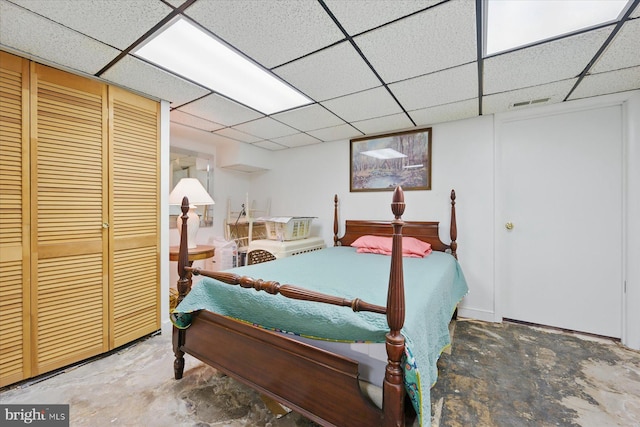 bedroom with unfinished concrete floors, a paneled ceiling, and a closet