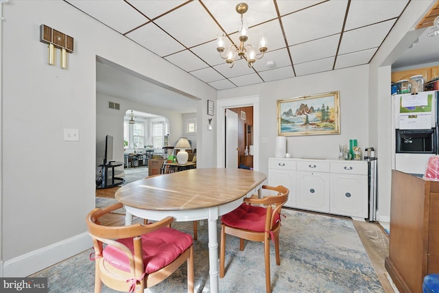 dining area featuring a chandelier, a paneled ceiling, arched walkways, baseboards, and light wood-type flooring