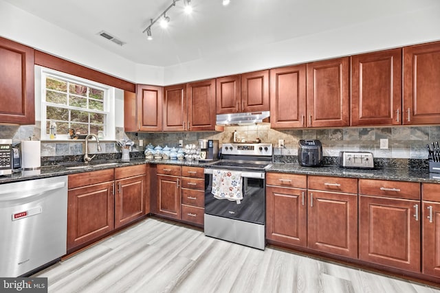 8328 Ridge View Rd, Lusby, MD 20657 - kitchen featuring appliances with stainless steel finishes, a sink, under cabinet range hood, light wood finished floors, and dark stone counters