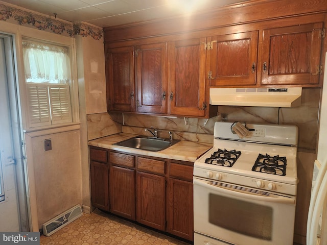 841 Highland Ave, Lancaster, PA 17603 - kitchen with white gas range, under cabinet range hood, a sink, light countertops, and brown cabinetry
