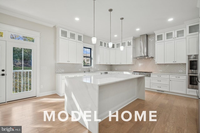kitchen featuring wall chimney exhaust hood, appliances with stainless steel finishes, white cabinets, a sink, and a center island