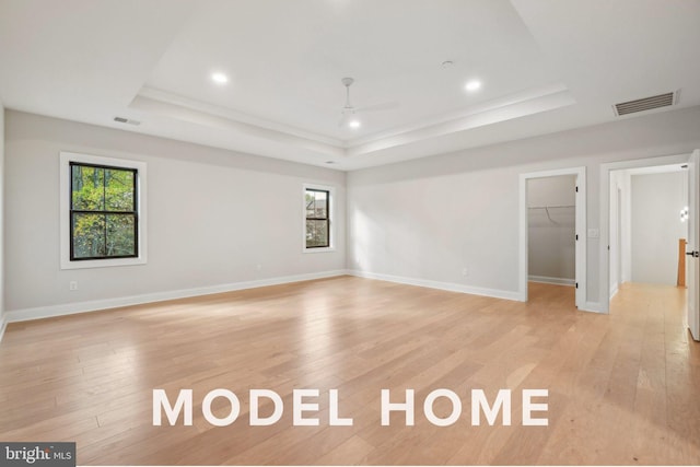 spare room featuring a tray ceiling, ceiling fan, light wood-type flooring, recessed lighting, and baseboards