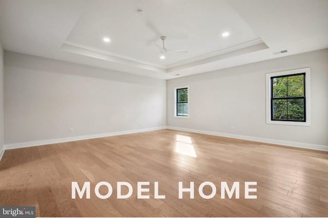 spare room featuring a raised ceiling, light wood finished floors, a ceiling fan, recessed lighting, and baseboards