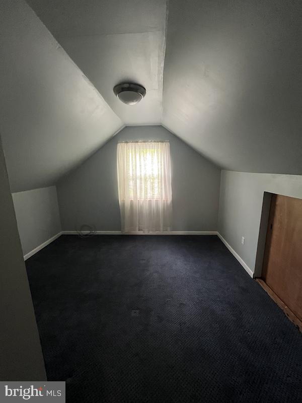 additional living space featuring vaulted ceiling, baseboards, and dark colored carpet