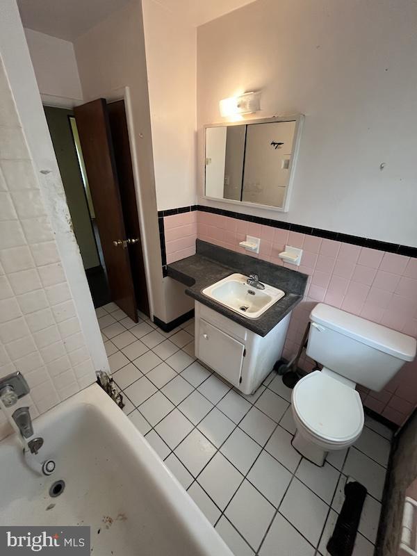 bathroom featuring tile walls, tile patterned floors, a wainscoted wall, toilet, and vanity